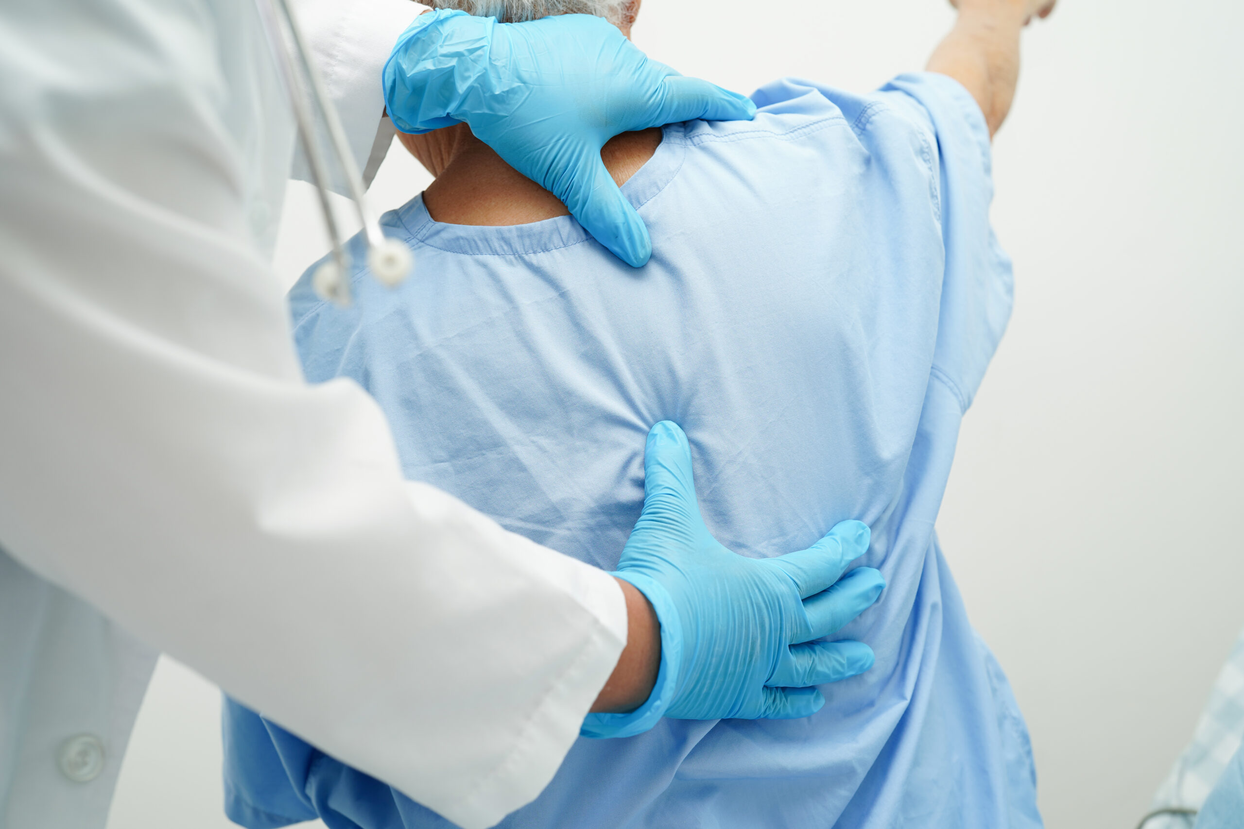 Clinician wearing gloves examining an older patient's back during an exam