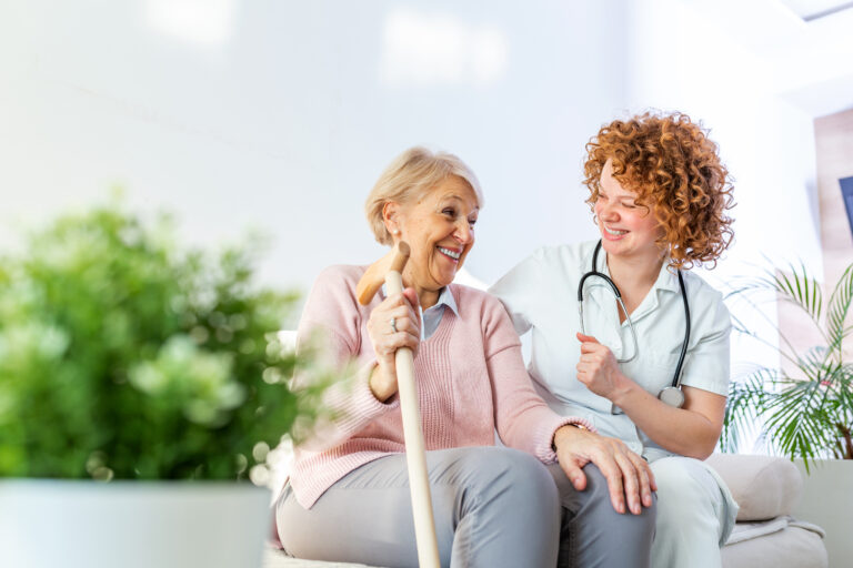 Smiling older patient with a cane sitting beside a smiling clinician